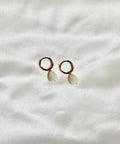 Pair of earrings with circular tops and teardrop-shaped stones on a white fabric background