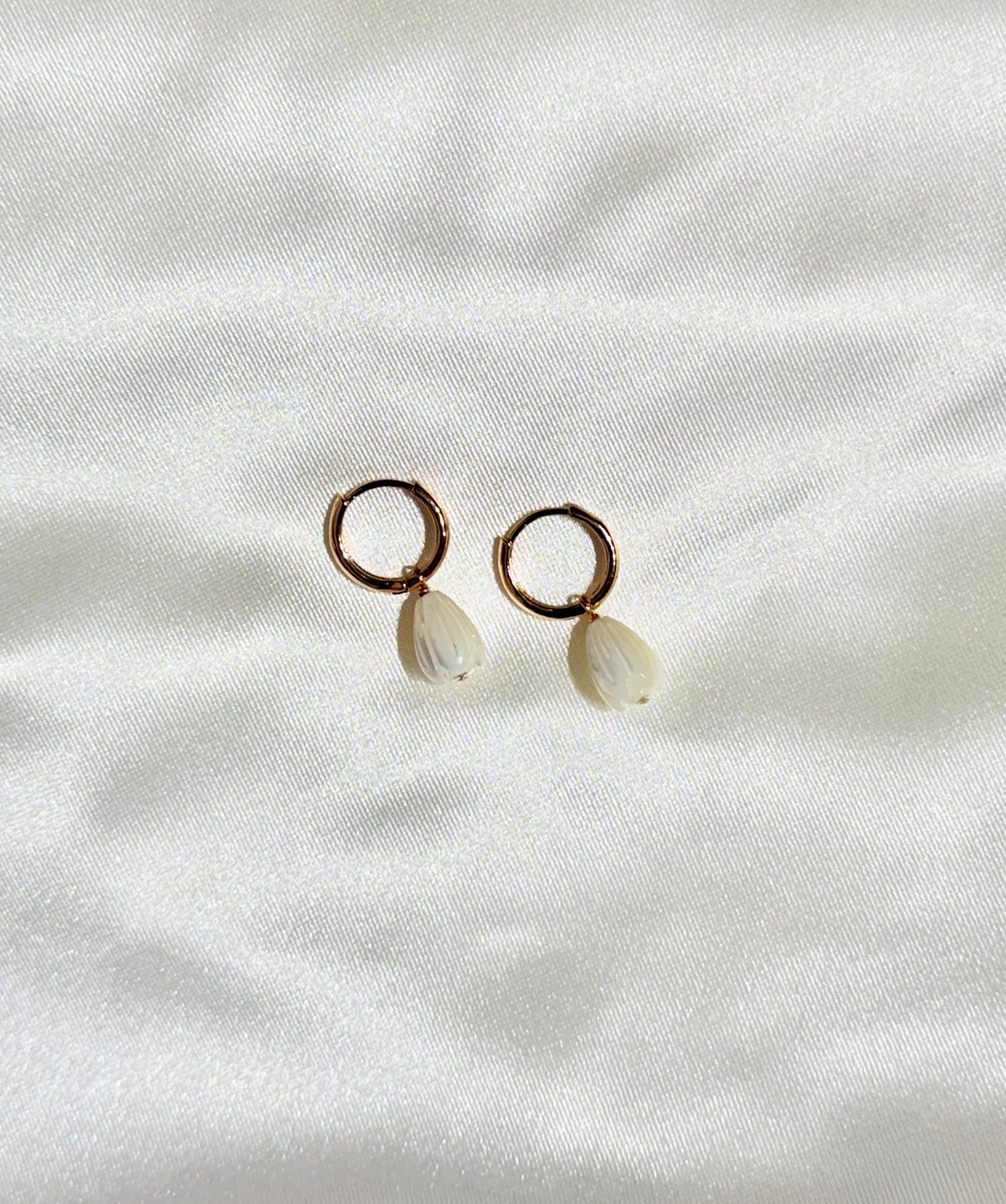 Pair of earrings with circular tops and teardrop-shaped stones on a white fabric background
