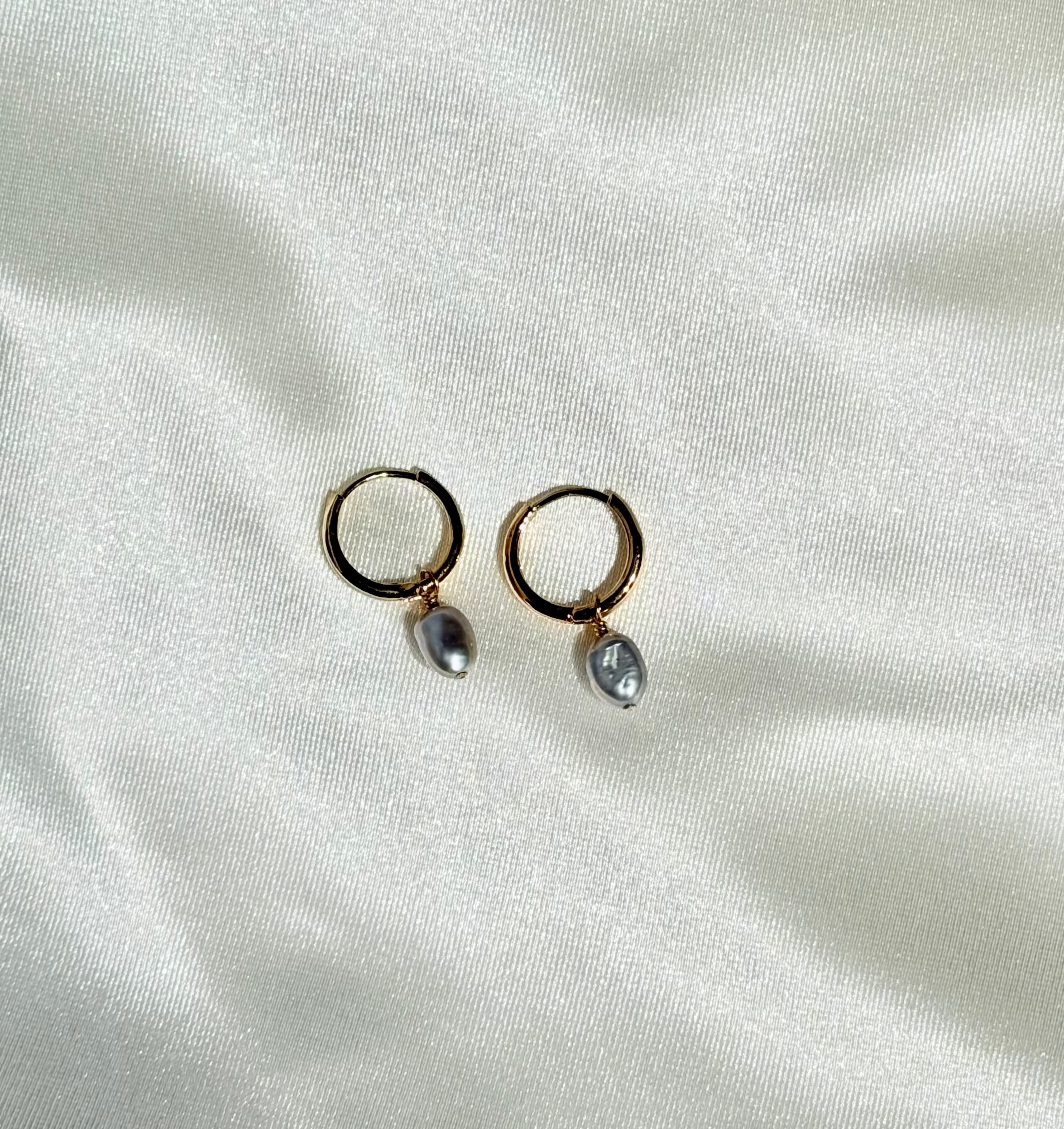 Pair of gold hoop earrings with small pearls on a white fabric background