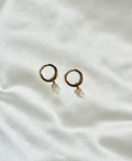 Gold hoop earrings with pearl drops on a white fabric background