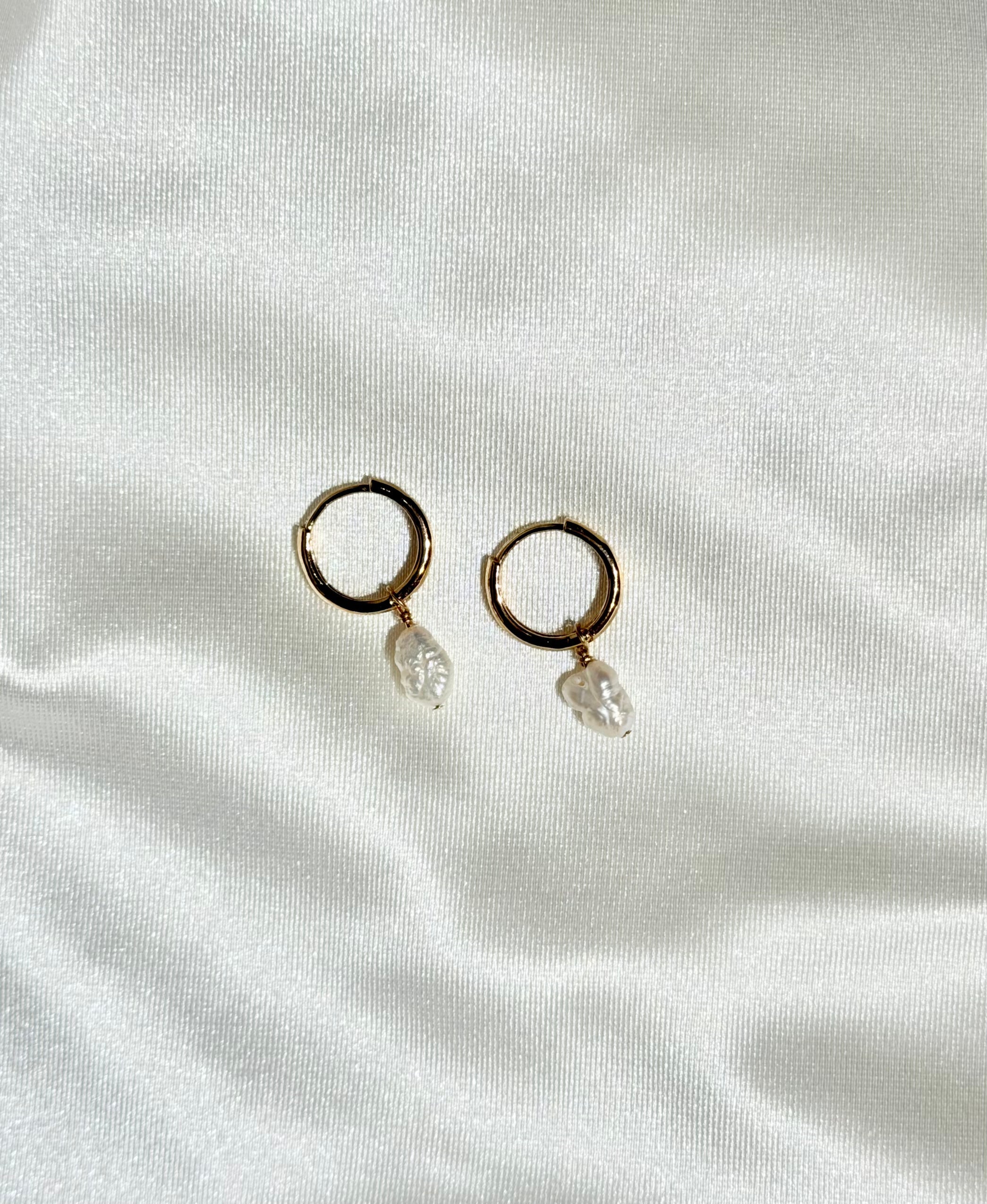 Gold hoop earrings with pearl drops on a white fabric background