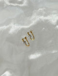 A pair of 14k gold-filled chain loop earrings with a gray keshi pearl, displayed on white satin fabric in natural light.
