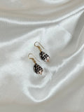 Hebrew cone shell earrings with natural spotted pattern and gold hardware on white fabric