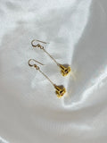 Gold puakenikeni flower earrings with delicate chain drops on white fabric