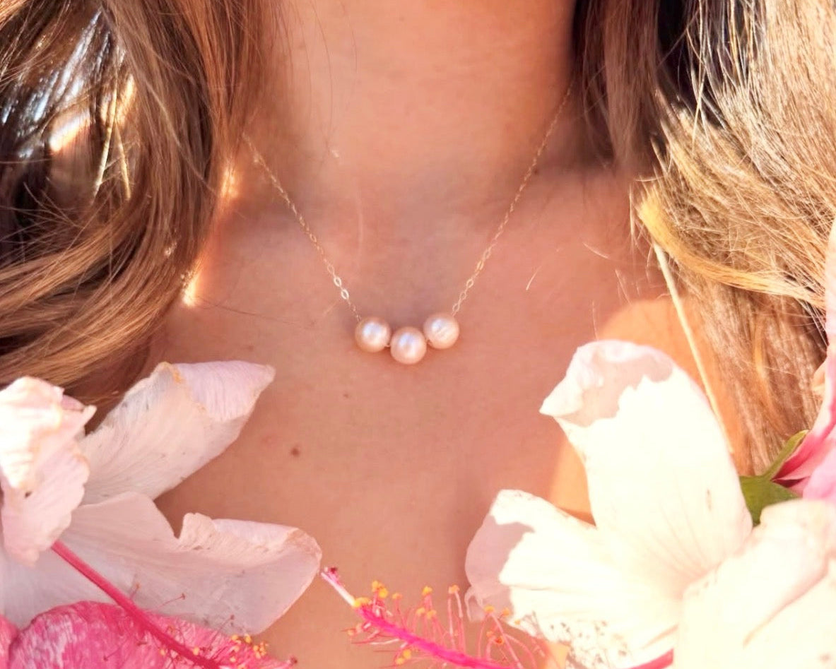 Three white freshwater pearls centered on delicate gold chain necklace worn on neck