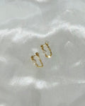 A pair of 14k gold-filled chain loop earrings with a white keshi pearl, displayed on white satin fabric in natural light.